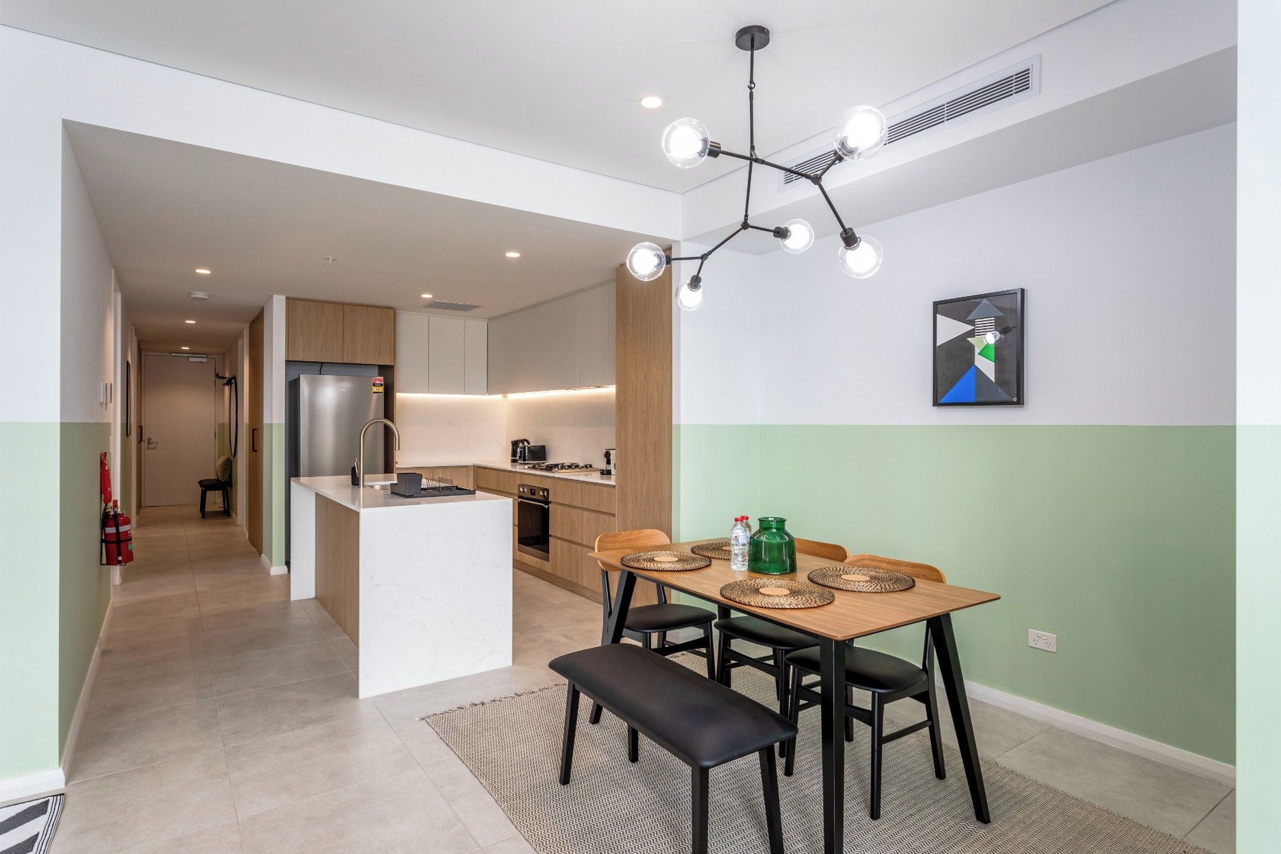 Une cuisine moderne dotée d’un îlot central, d’un coin repas avec un banc et d’un luminaire contemporain.