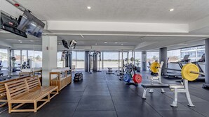 Un gimnasio con equipamiento de ejercicio, bancos y un ventanal que ofrece vistas al exterior.