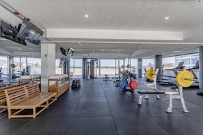 Een sportschool met trainingsapparatuur, banken en een groot raam met uitzicht op buiten.