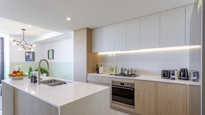 A modern kitchen with a central island, stainless steel appliances, and a light wood finish cabinetry. - KULA Wollongong (Wollongong)