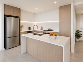 A modern kitchen with a stainless steel refrigerator, a sink, and a countertop with a fruit bowl.