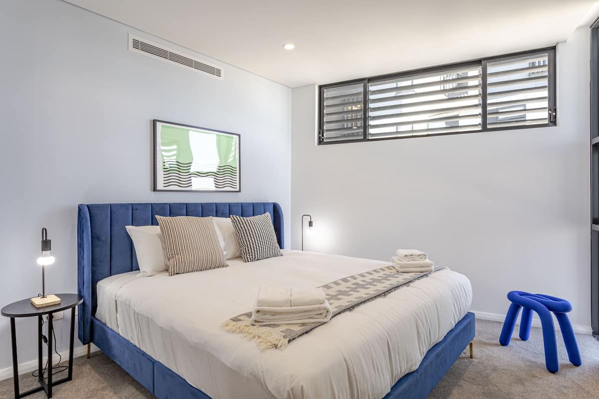 Un dormitorio moderno con una cama grande, una mesita de noche, un cuadro colgado en la pared y una ventana con persianas.