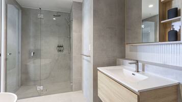 A modern bathroom with a glass-enclosed shower, a white sink, and a large mirror.