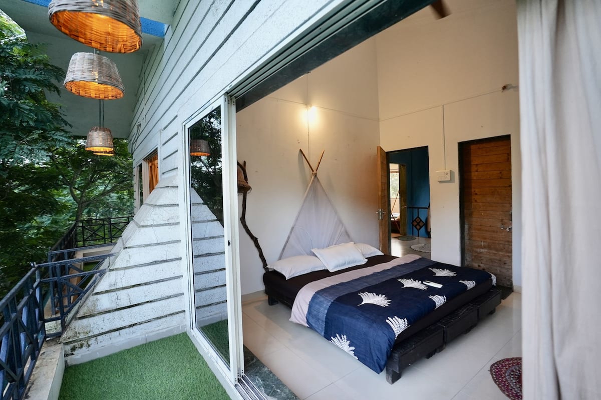 A bedroom with a bed, a window, and a staircase leading to an outdoor area.