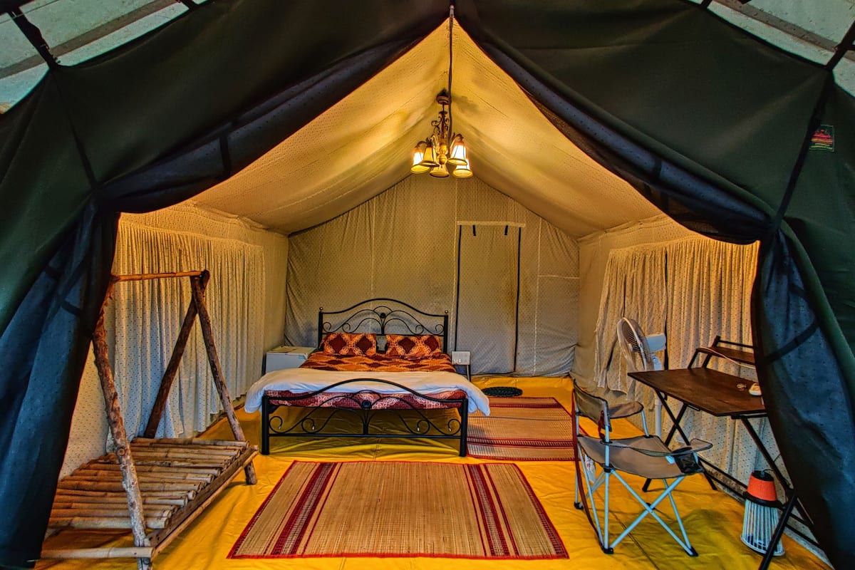 A tent with a bed, a chair, a table, and a hanging light fixture.
