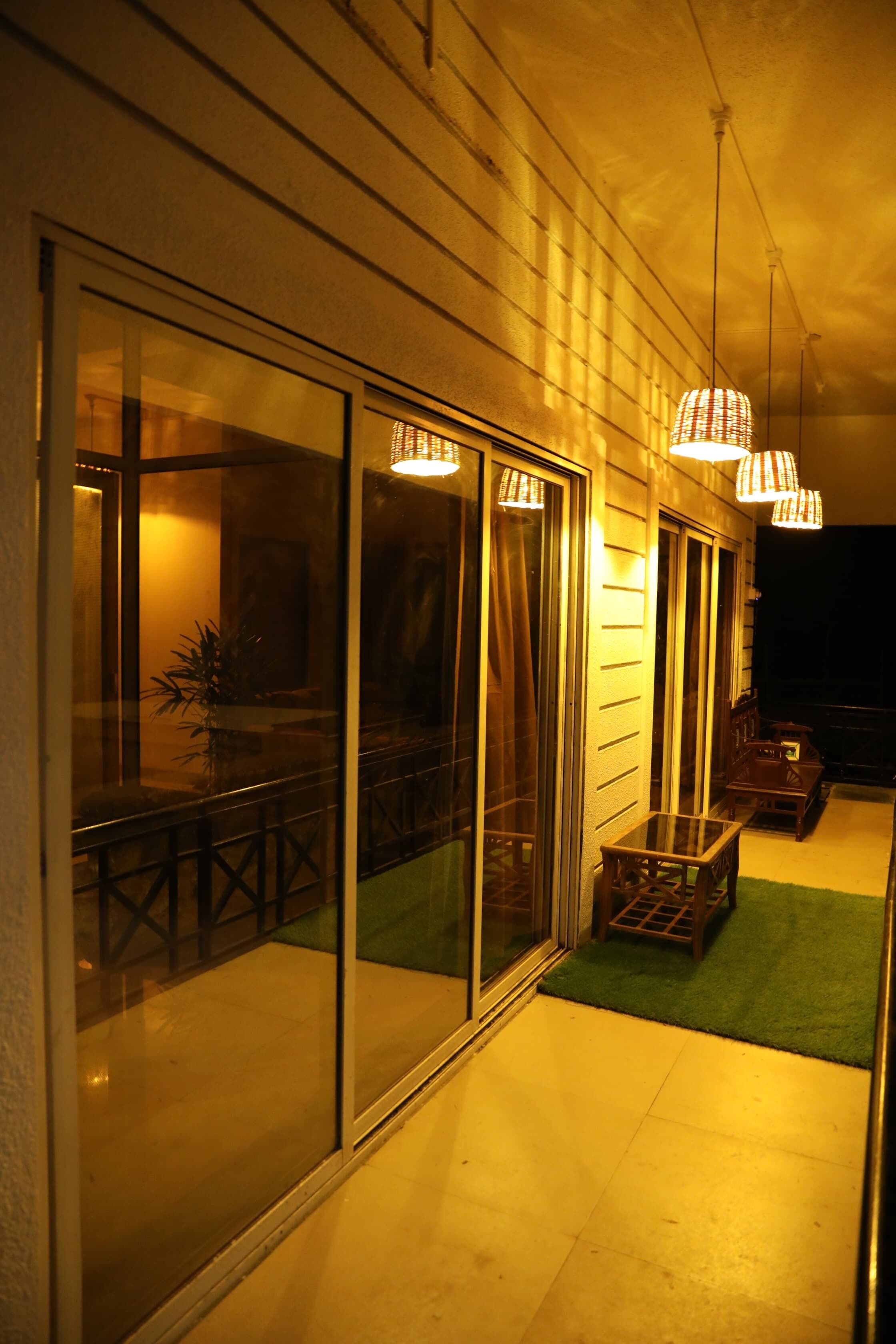 A corridor with sliding glass doors, a small seating area with a table and chairs, and hanging pendant lights.
