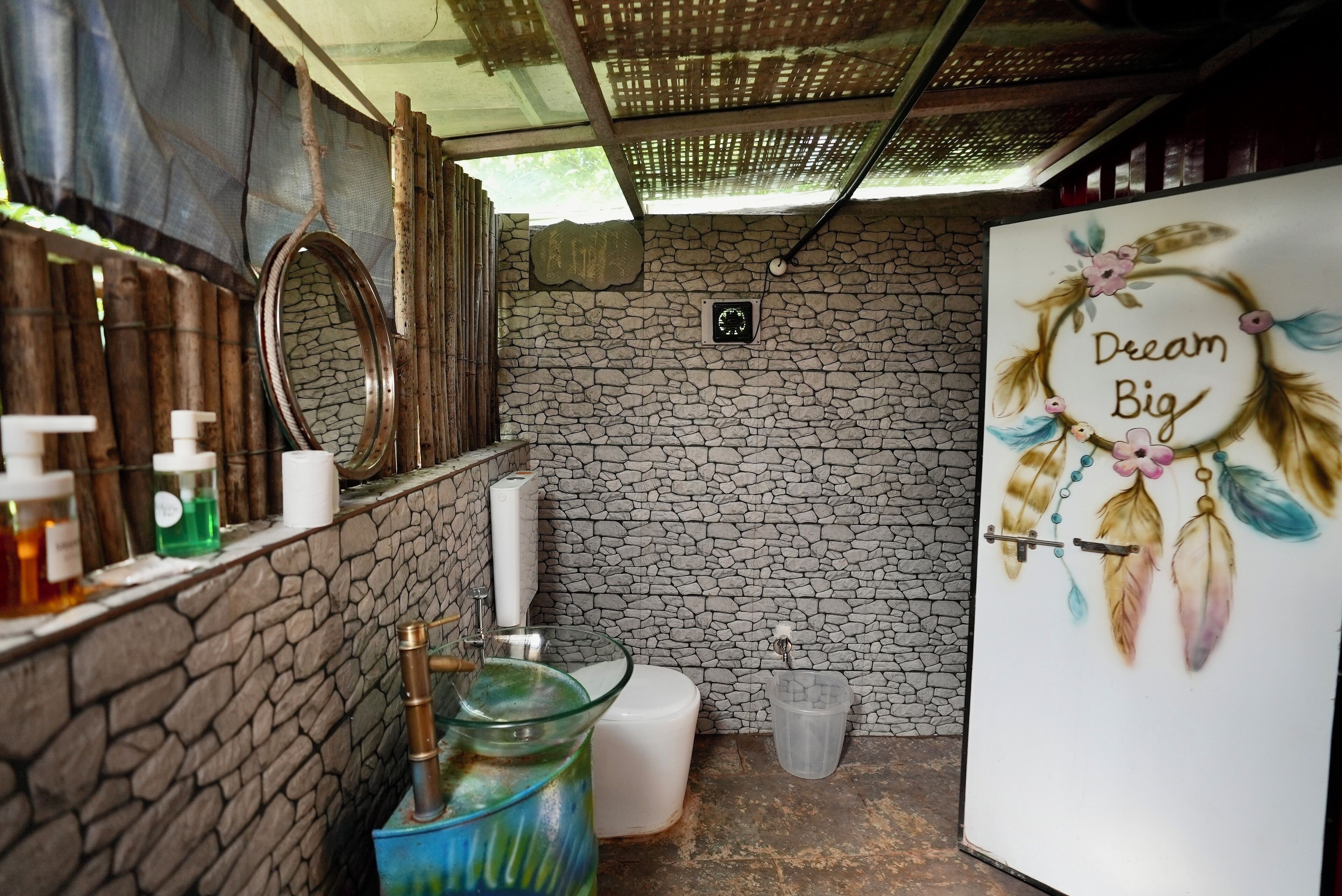 A bathroom with a stone wall, a mirror, a toilet, and a sink with toiletries.