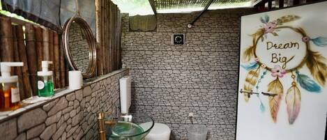A bathroom with a stone wall, a mirror, a toilet, and a sink with toiletries.