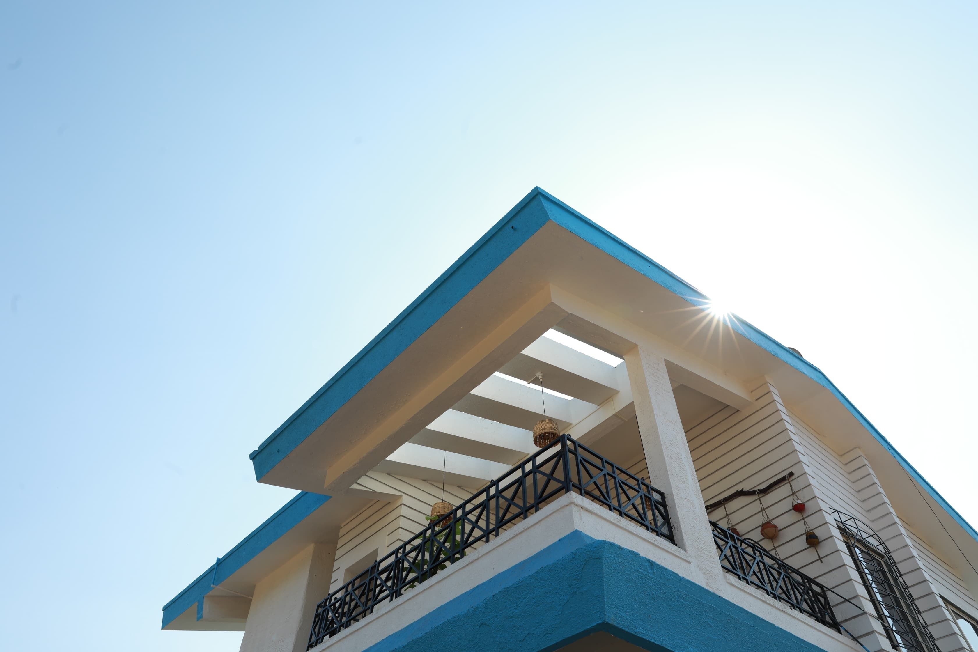 Un bâtiment à la façade bleue et blanche, doté d’un balcon avec des balustrades noires, et un ciel dégagé.