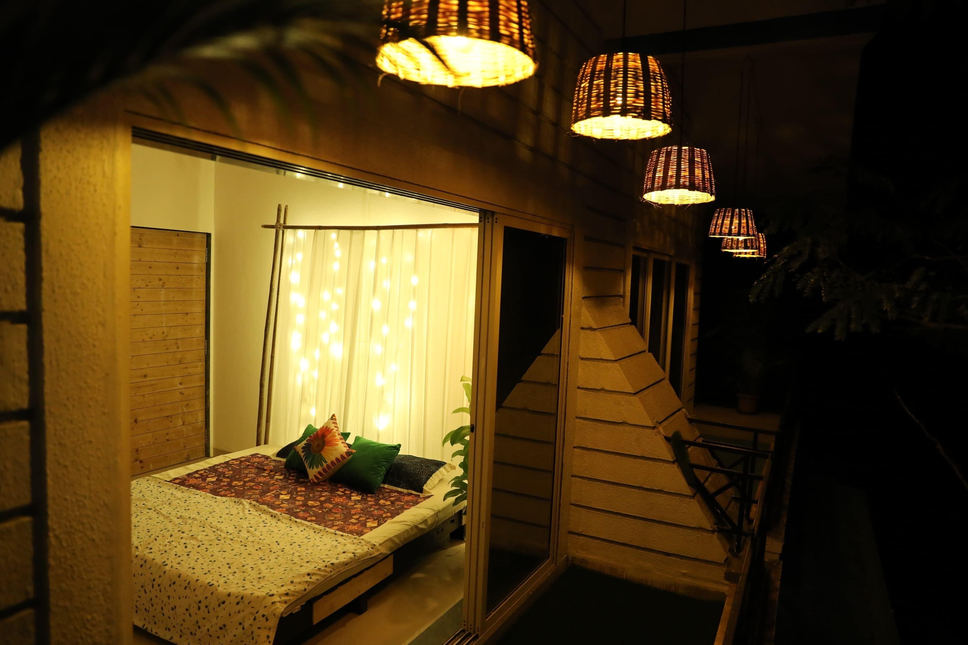 A cozy bedroom with a bed, a window with curtains, and hanging lights.