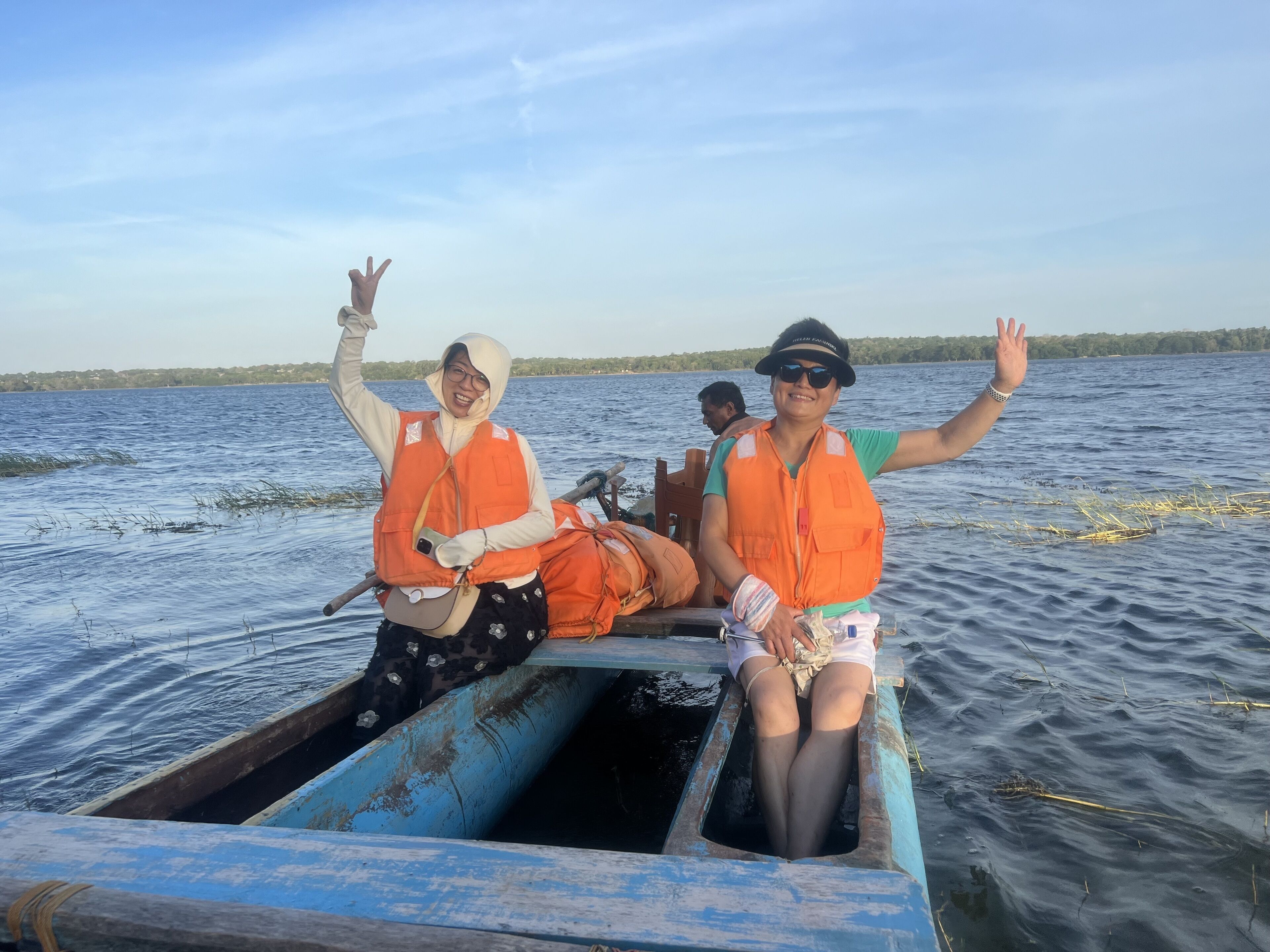 Un bote con dos personas que llevan chalecos salvavidas anaranjados, una alzando la mano.