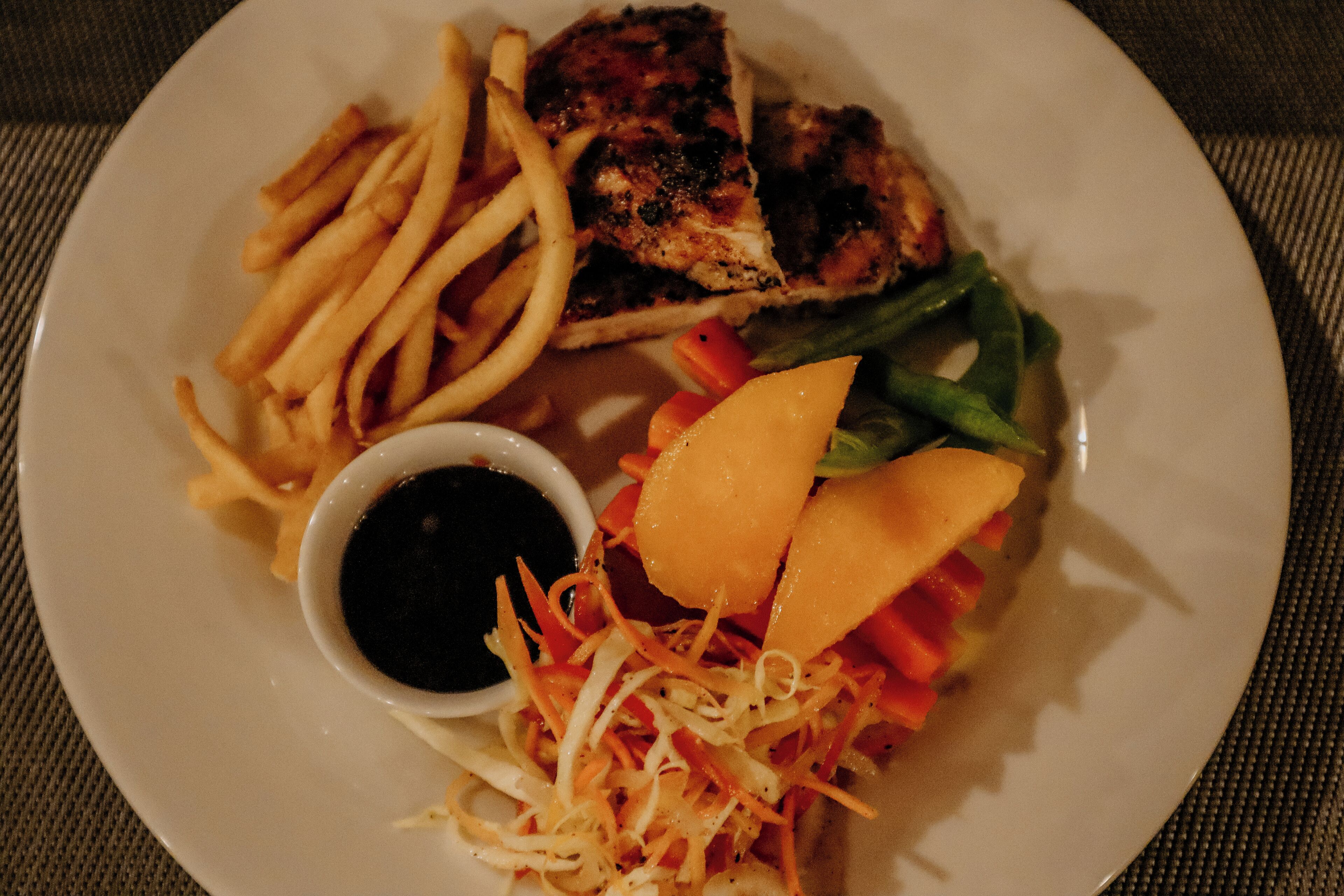 Ein Teller mit gegrilltem Hähnchen, Pommes Frites, Salat und einer kleinen Soße.