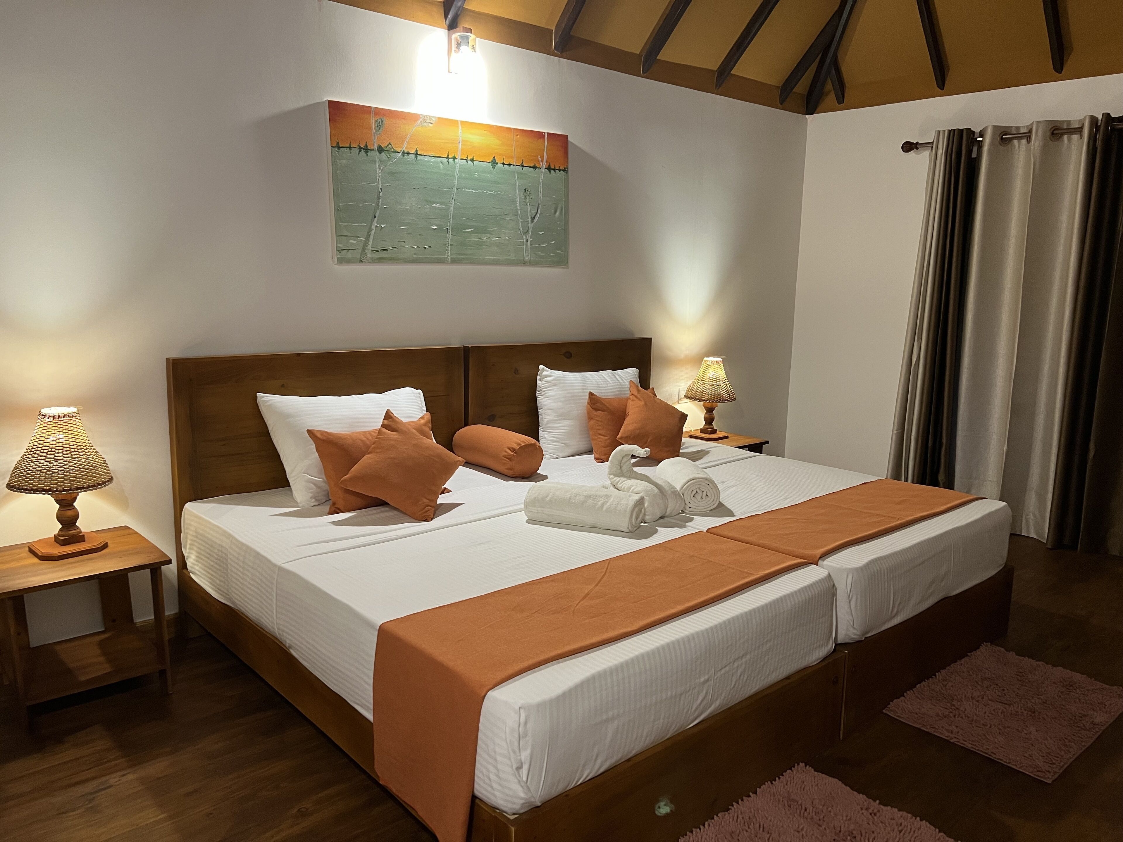 A double bed with a wooden headboard, two bedside tables with lamps, a painting on the wall, and a window with curtains.