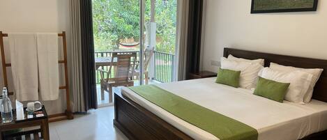 A hotel room with a large bed, a wooden headboard, a green throw blanket, and a view of the outdoors through a sliding glass door.