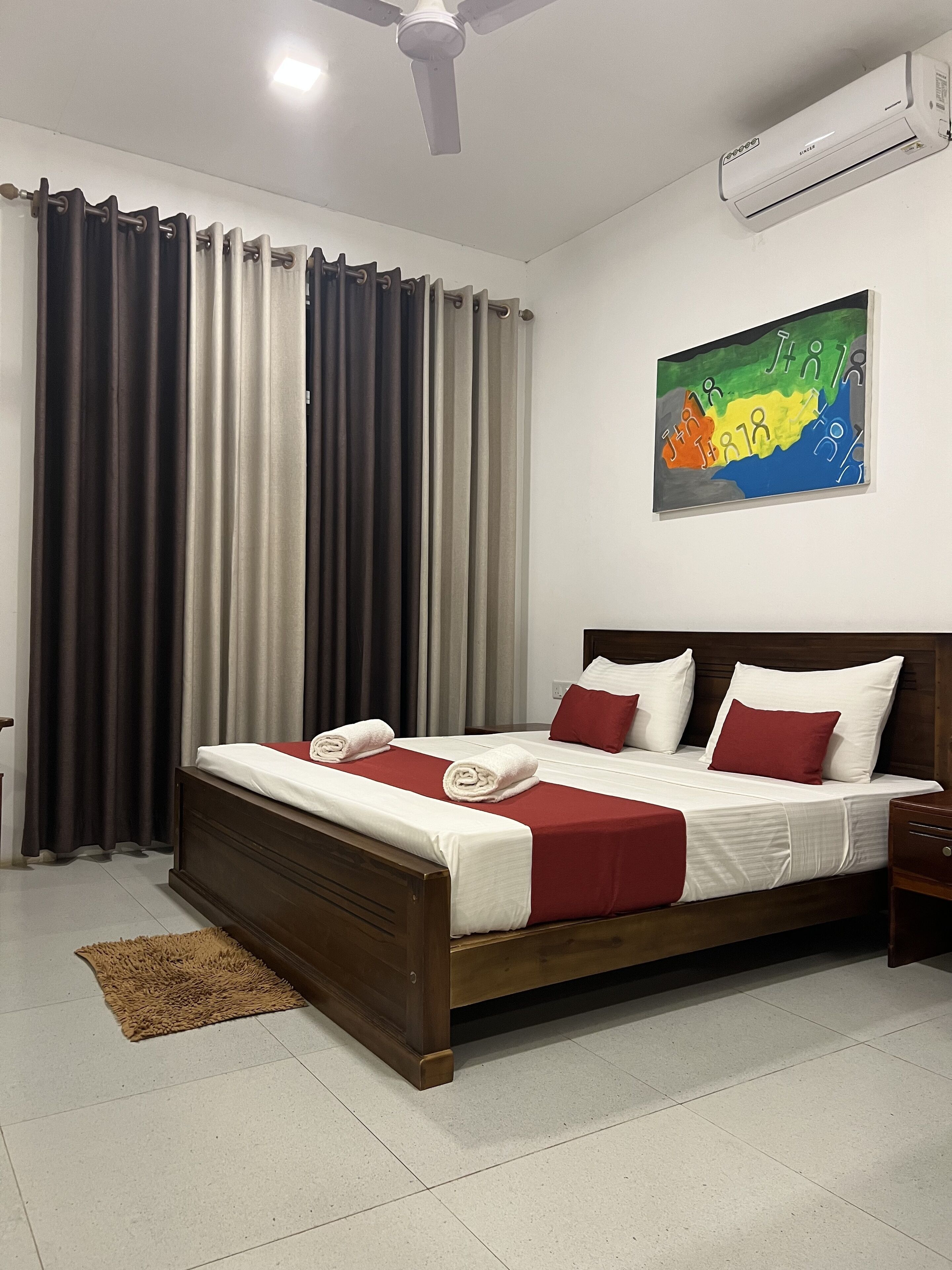 A neatly made bed with red and white bedding, a wooden headboard, and a brown floor rug.