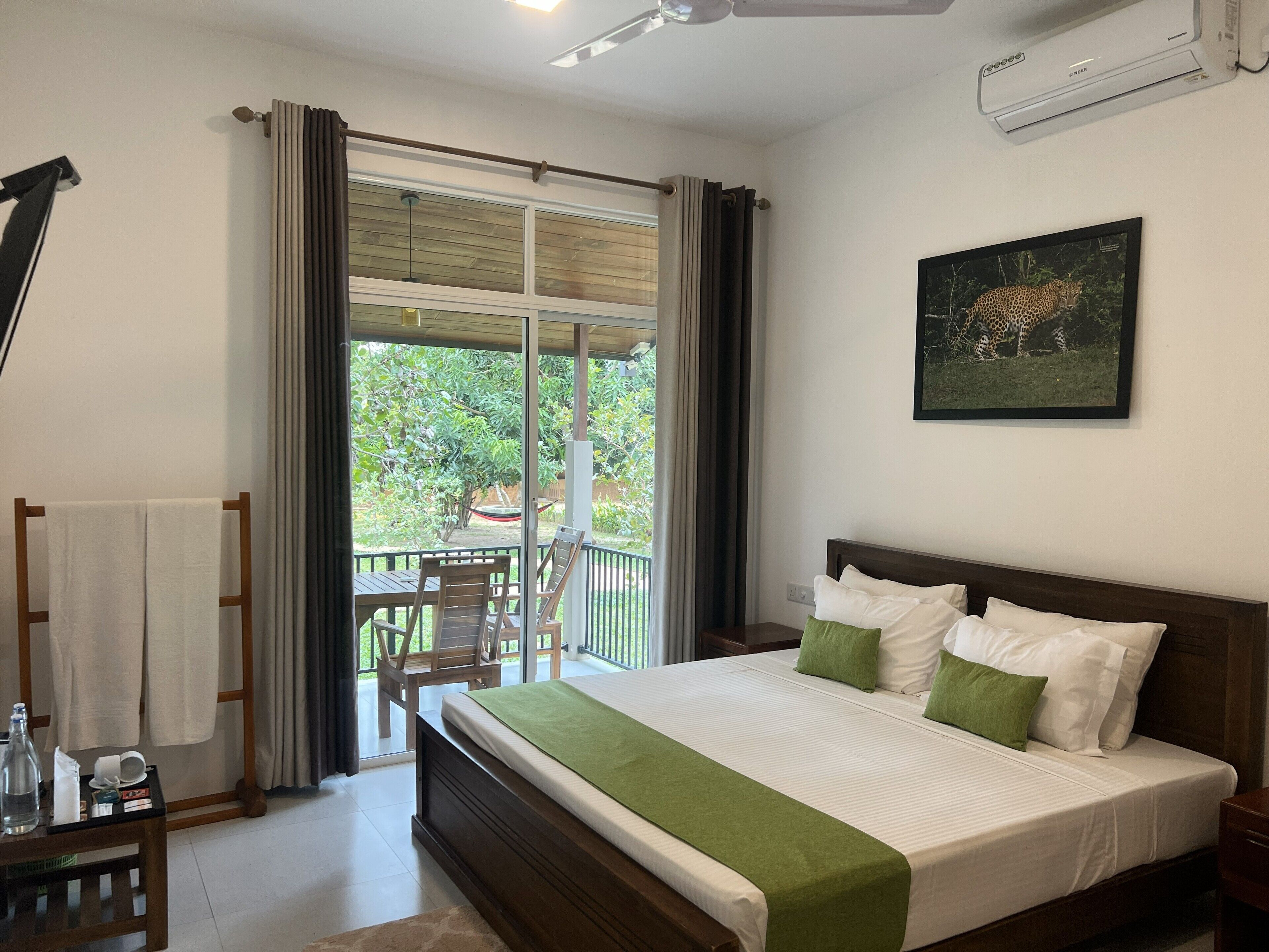 Habitación de hotel con una cama grande, un balcón con vistas a zonas verdes y un ventilador de techo.