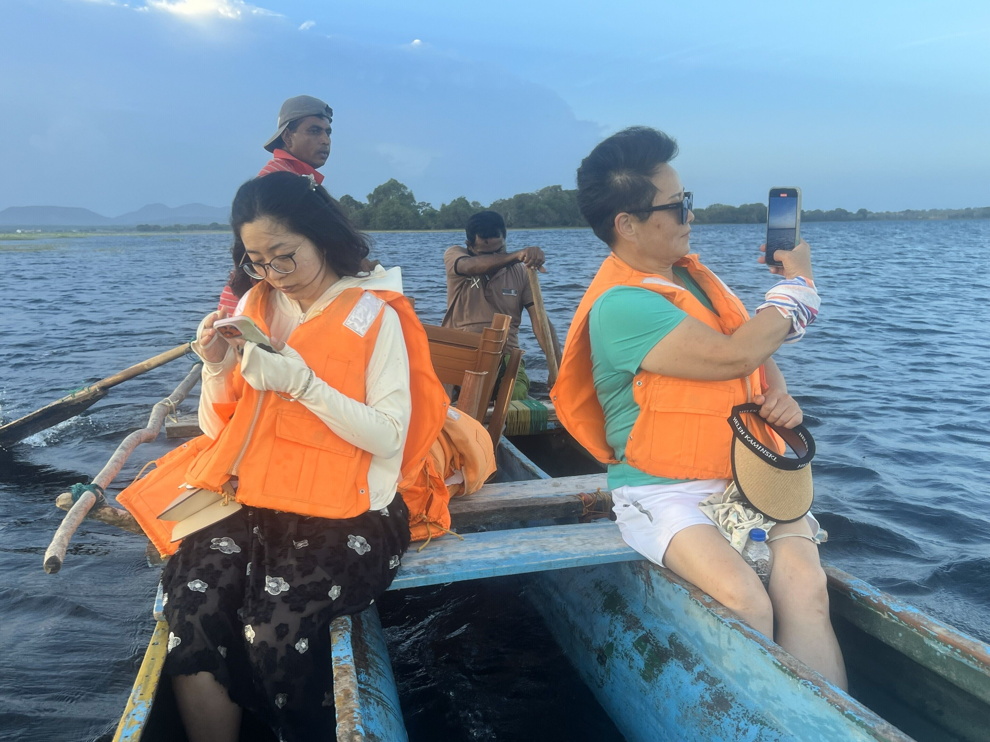 A group of people on a boat with a calm water body and distant land in the background.