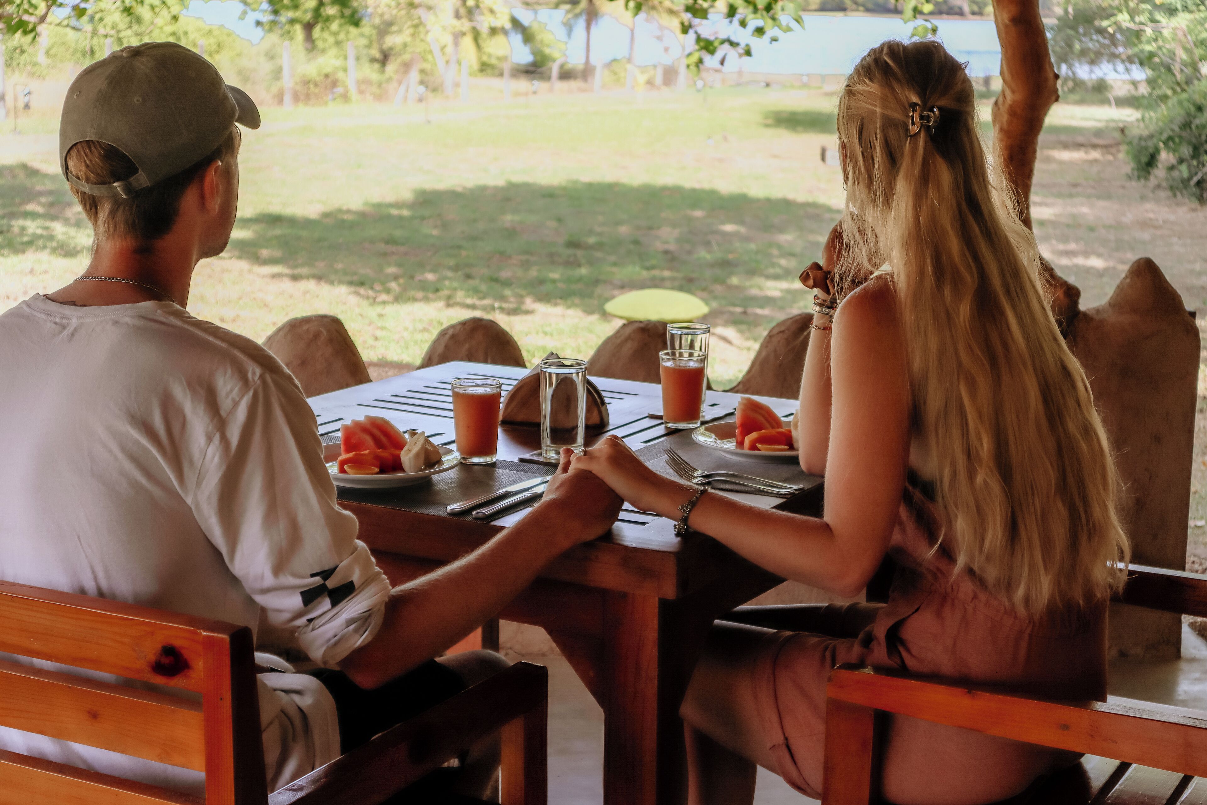 A couple dining at an outdoor table with a view of a grassy area and trees.