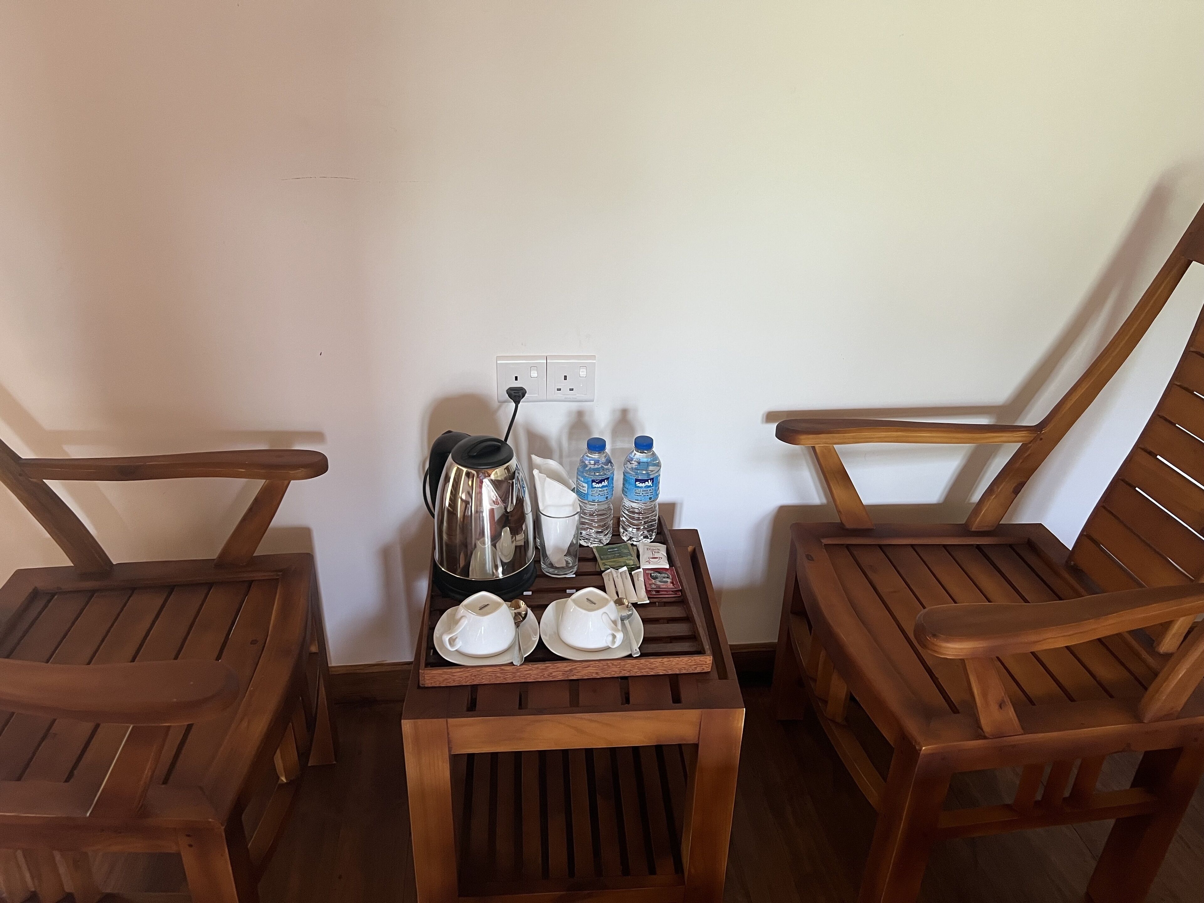A small wooden table with a kettle, two cups, two bottles of water, and a tissue box.