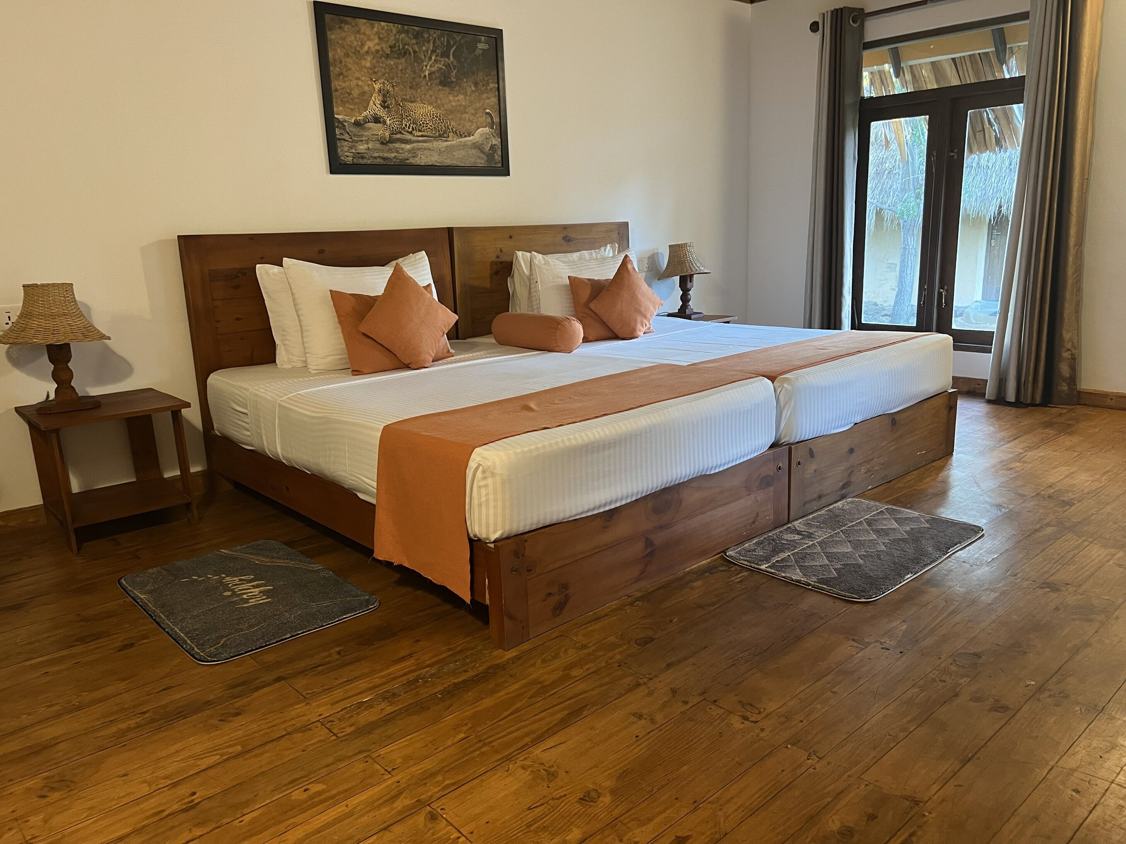 A wooden bed with a headboard, white bedding, and multiple pillows. There is a small table with a lamp beside the bed, and a rug on the floor.