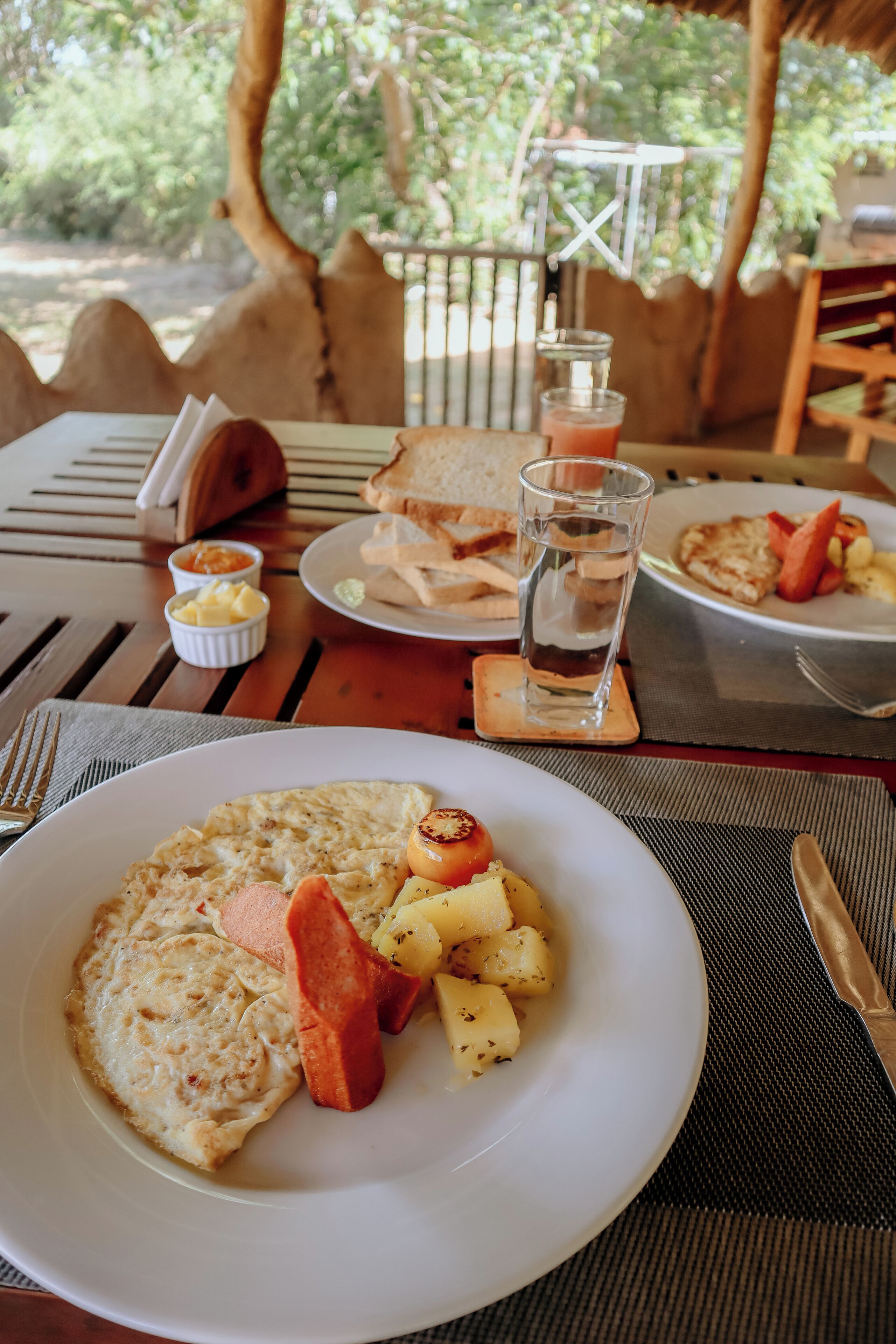 A breakfast table with plates of food, a glass of water, and a napkin holder.