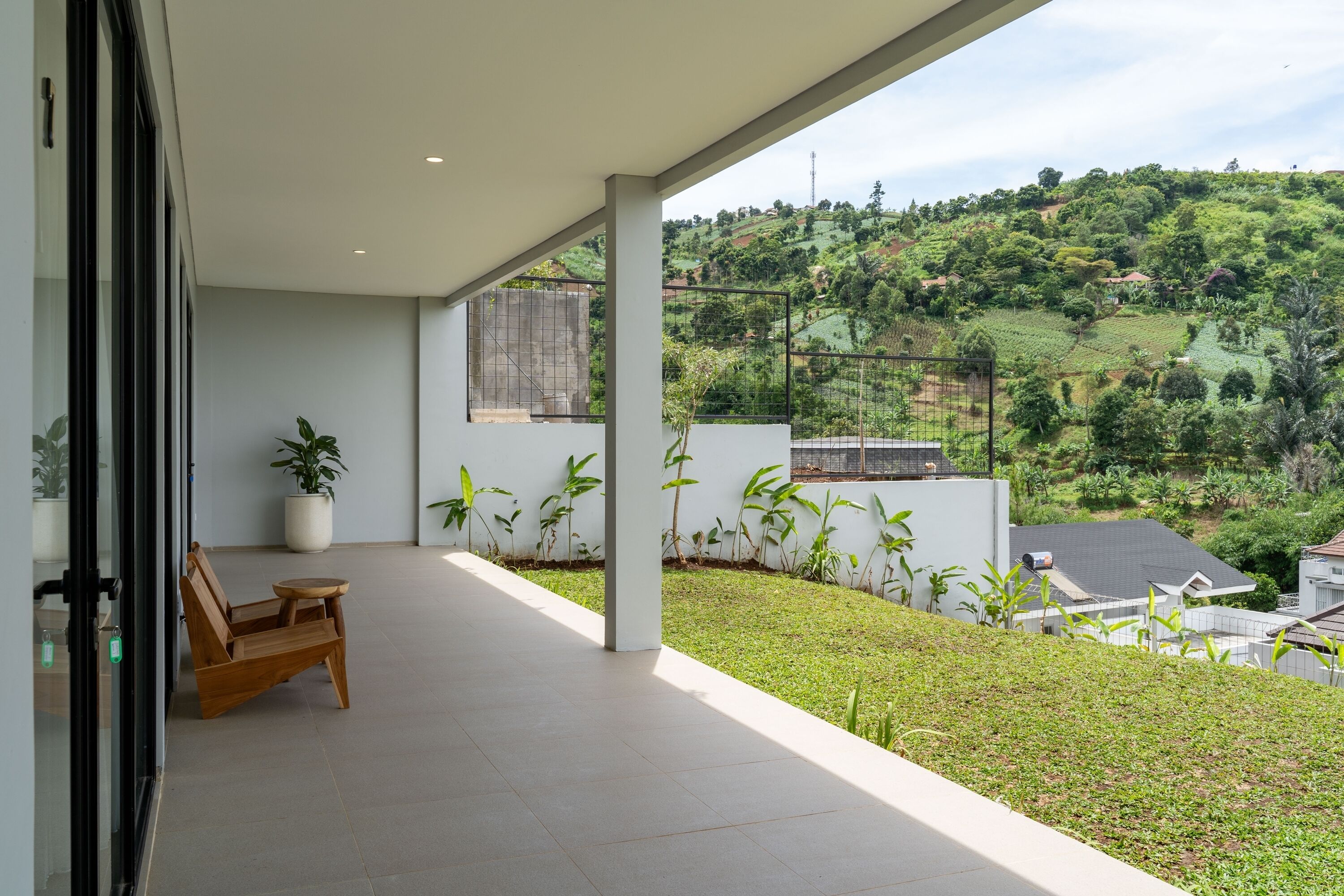 Un balcon avec une chaise en bois, des plantes en pot et une vue sur un paysage vallonné.