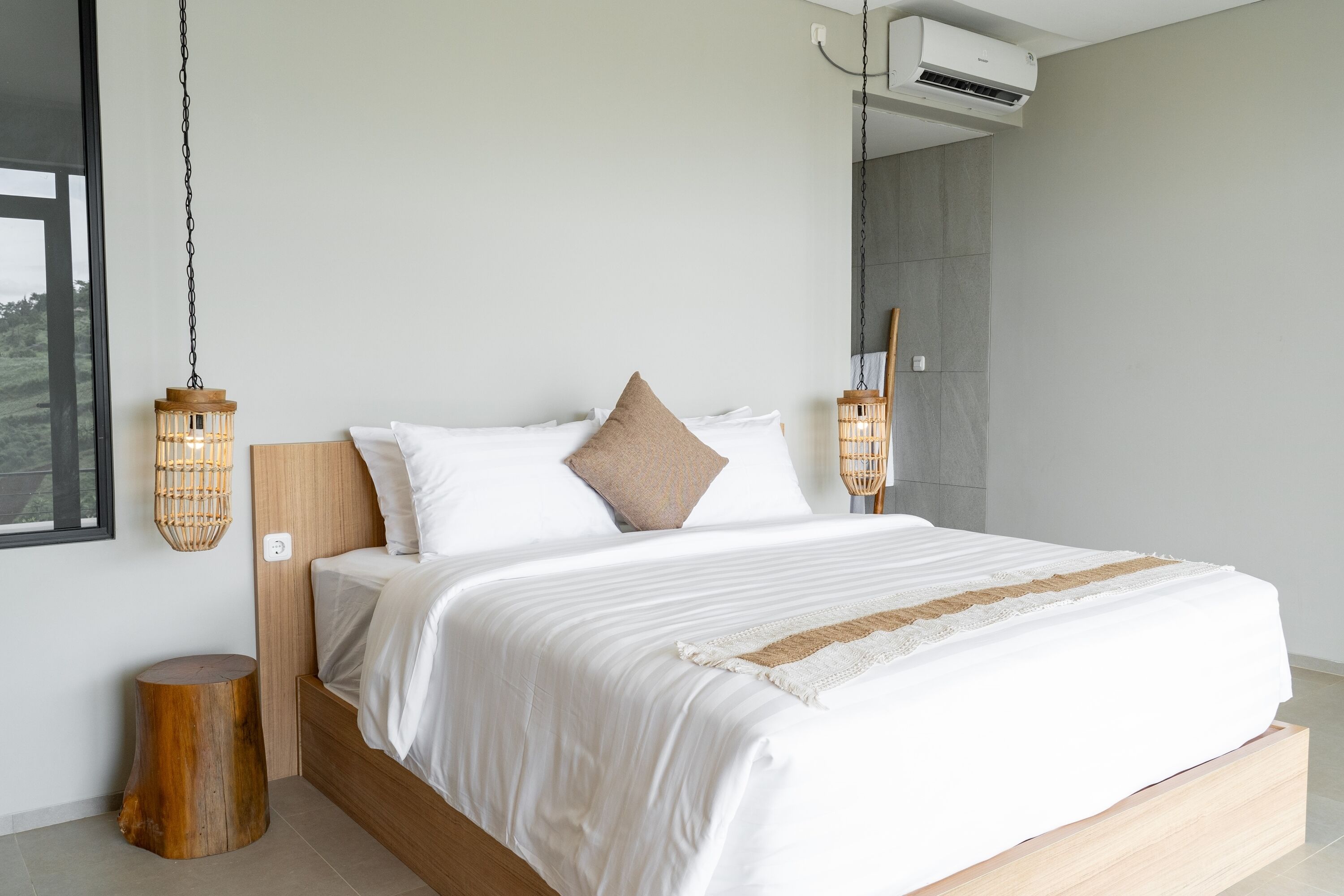 A modern bedroom with a large bed, white bedding, and two hanging lanterns.