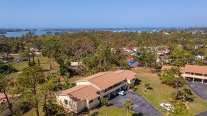 A large, single-story building with a flat roof, surrounded by dense trees and a clear view of the ocean. - Near Beaches! UPDATED! Peaceful Forest Park Condo 2 bd 2 bth. Heat comm pool (Englewood)