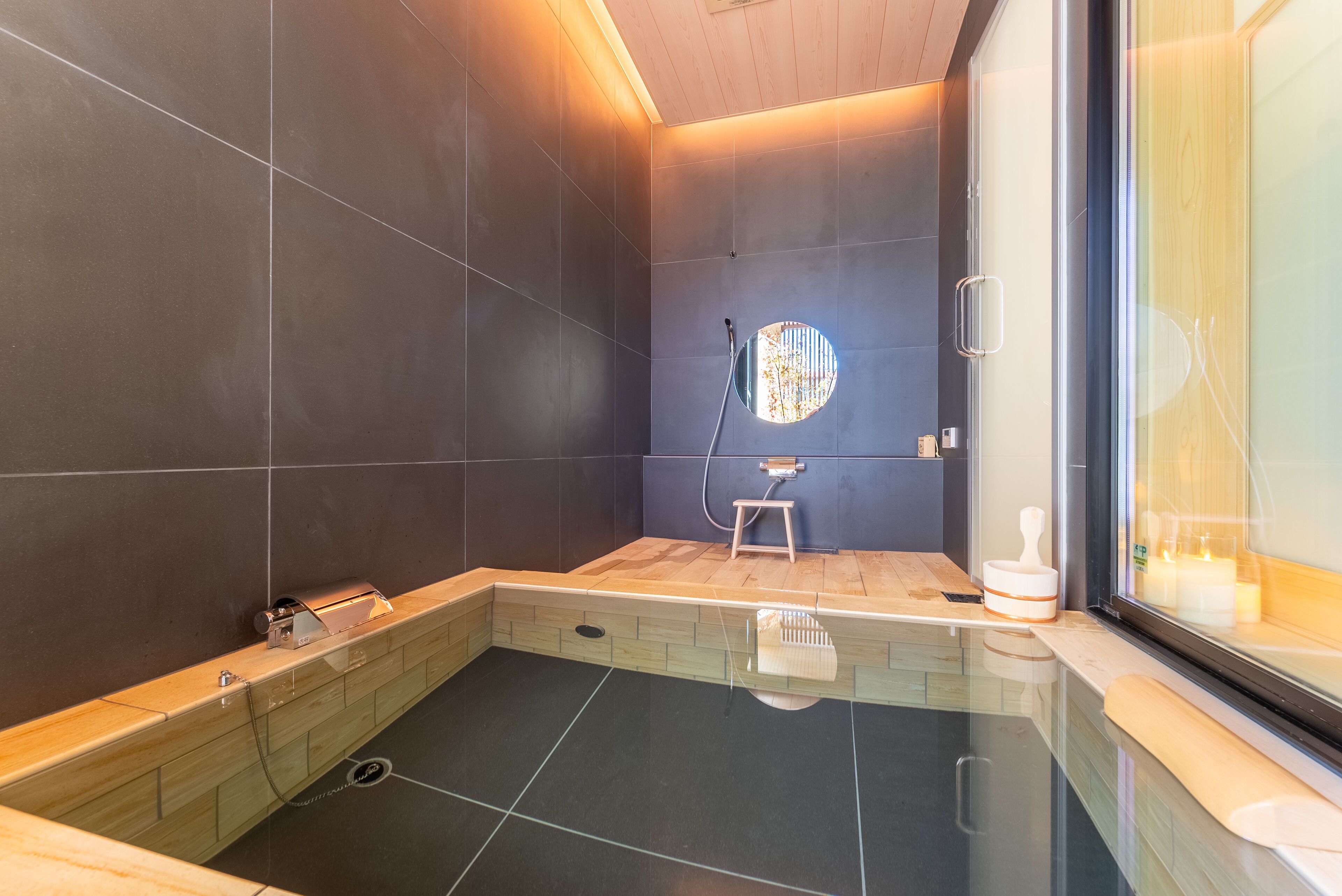 A modern bathroom with a glass shower enclosure, a wooden bench, and a small stool.