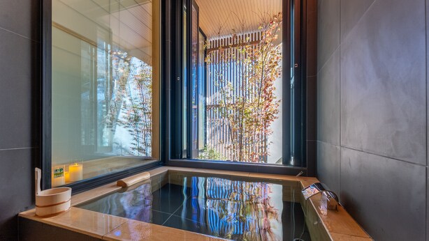 Un'area spa moderna con vasca idromassaggio vetrata, panche in legno e vista su un giardino attraverso ampie finestre.