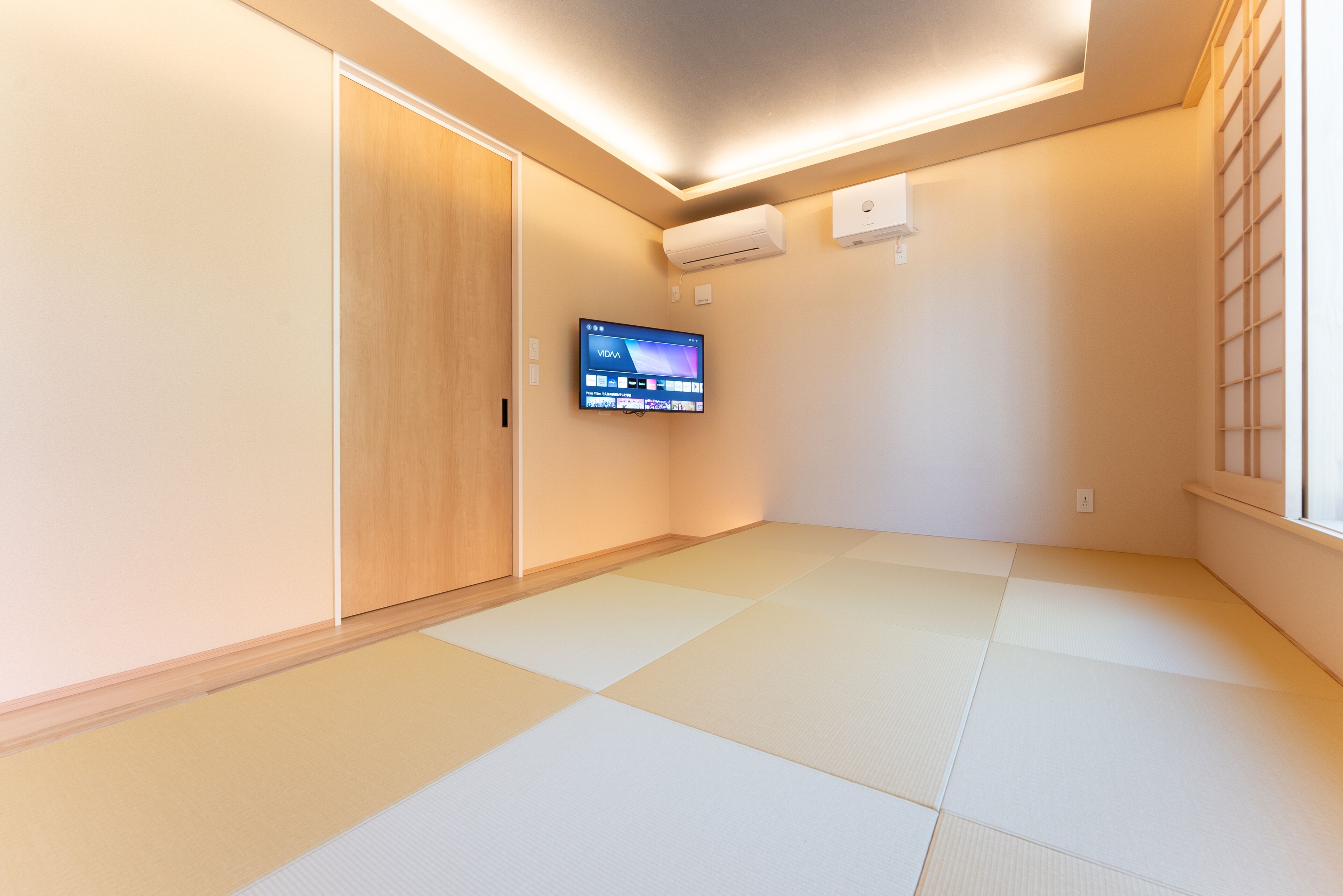 Una habitación con suelo de tatami, un televisor montado en la pared y una puerta corredera.