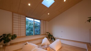 Una stanza con tatami, soffitto in legno basso, un lucernario e vista sul verde.