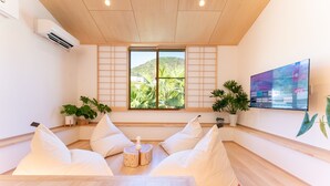 Una camera moderna con pavimento in legno, un'ampia finestra vista su spazi verdi, una TV a schermo piatto montata a parete e un piccolo tavolino con una bottiglia.