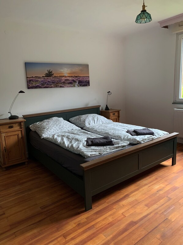 Ein Schlafzimmer mit einem hölzernen Bett, zwei Nachttischen, einer Wandlampe und einem Fenster mit Tageslicht.