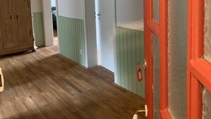 Un couloir avec un plancher en bois, une armoire en bois et une porte rouge.