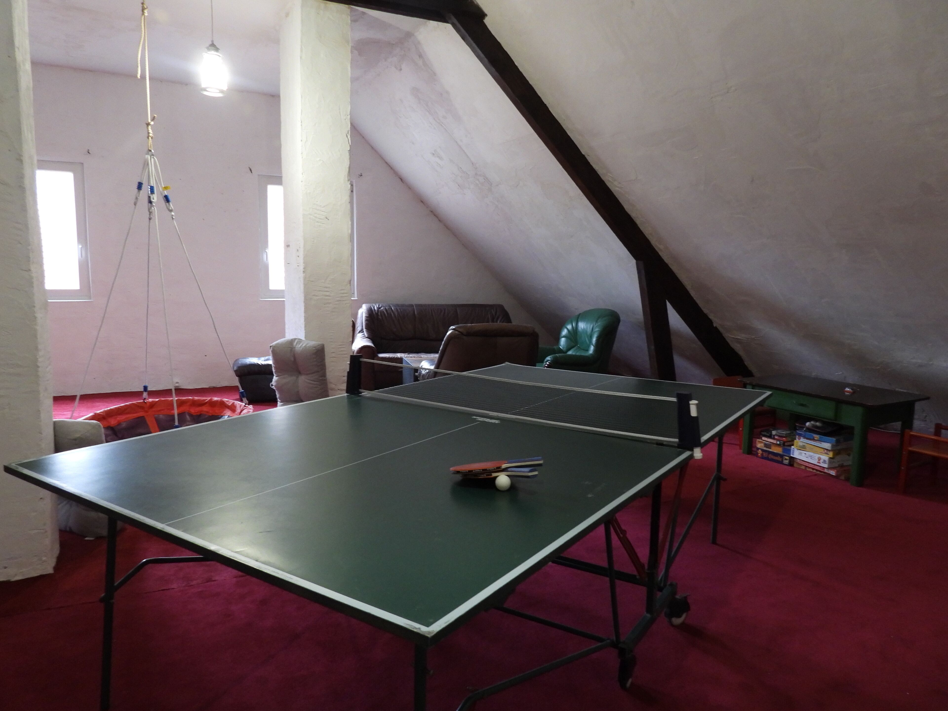 A ping pong table in a room with a sloped ceiling, red carpet, and a green chair.