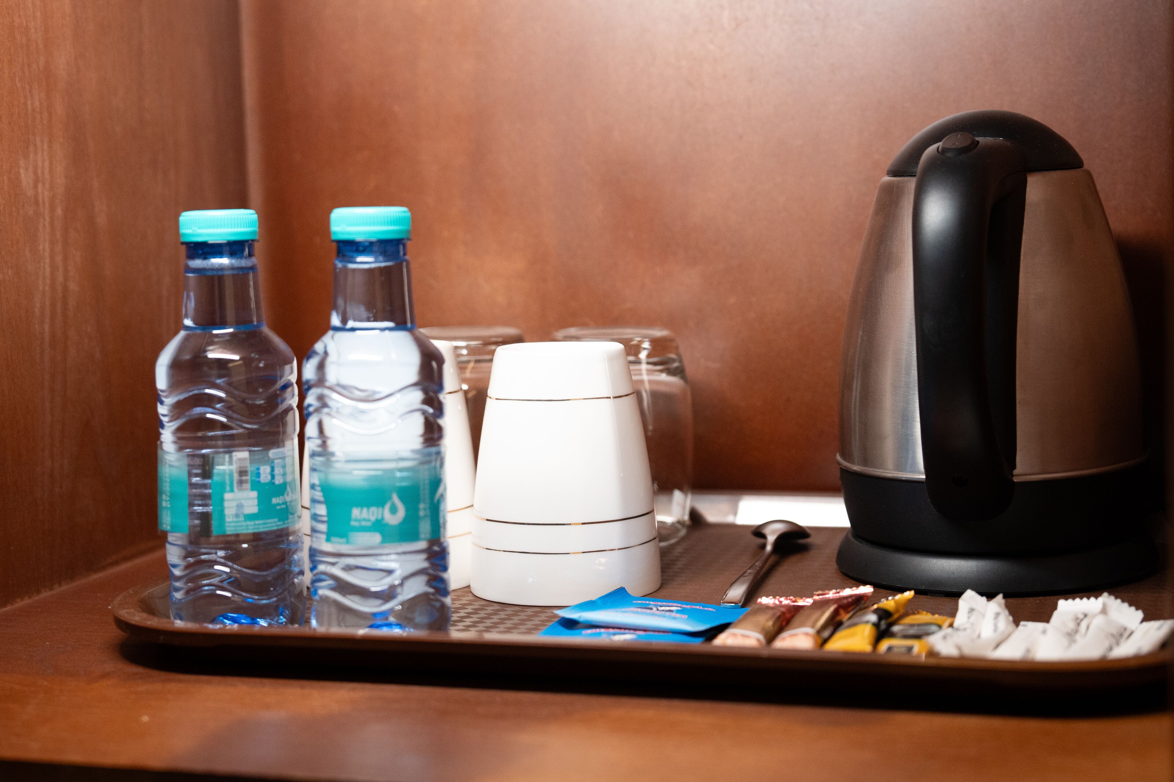 A tray with water bottles, a white mug, a black kettle, and some snacks.