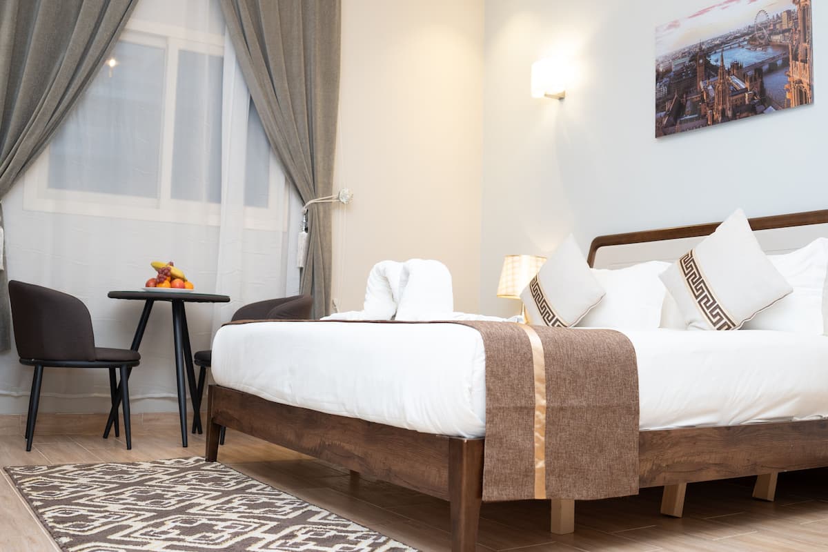 Una camera d'albergo con un letto, un tavolino con frutta, una sedia e vista sulla città.