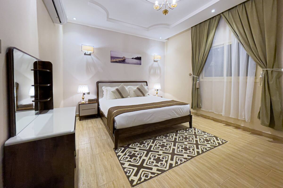Una camera d'albergo con un letto grande, un comodino, uno specchio, un lampadario e vista all'esterno dalla finestra.