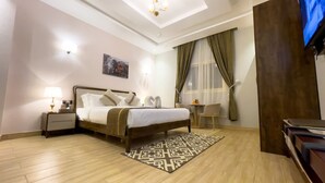 Habitación de hotel con cama, mesitas de noche, escritorio, silla, televisor y ventana con cortinas.