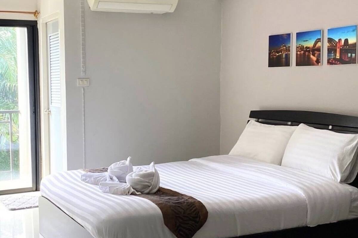 A modern hotel room with a large bed, a view of palm trees through the window, and three framed pictures on the wall.