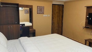 Habitación de hotel con cama, armario, escritorio, espejo, televisión y una pequeña mesa.