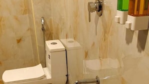 Un baño con inodoro, bidé y un balde en el suelo.