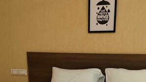 Una cama bien hecha con sábanas blancas en una habitación con pared color beige y un cartel enmarcado encima.