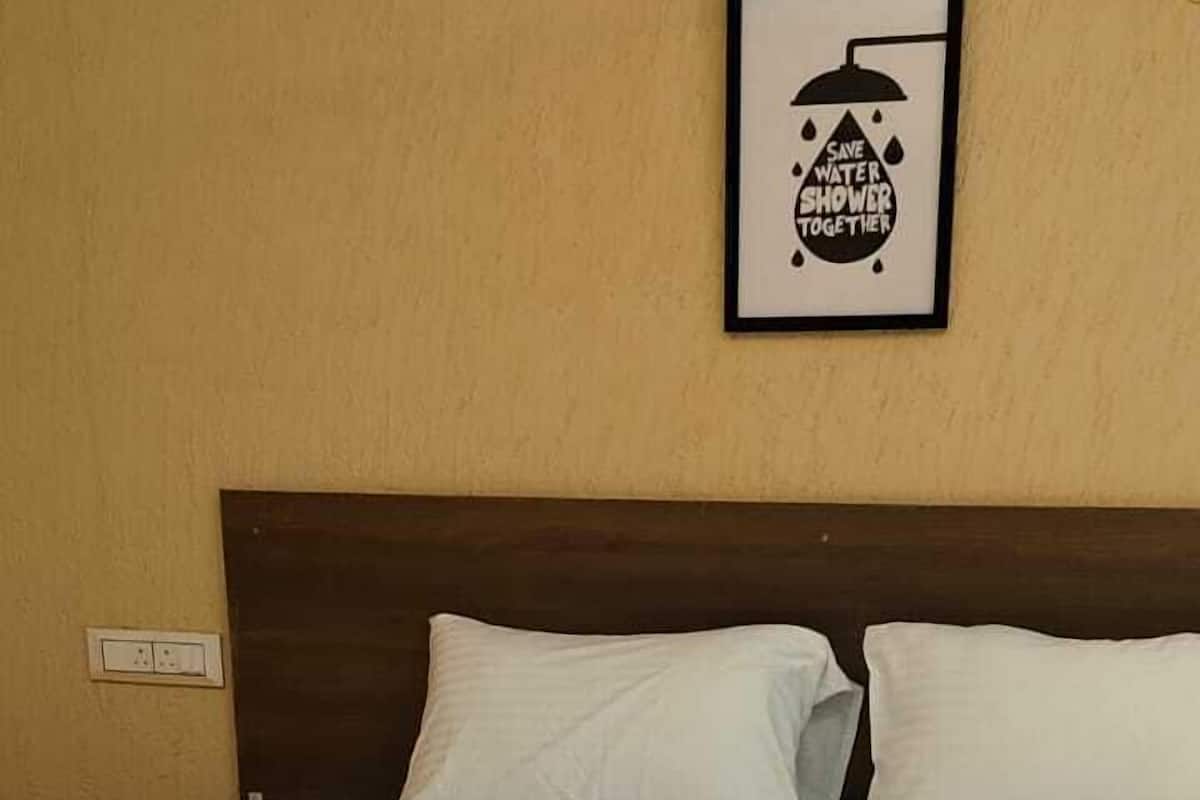 A neatly made bed with white linens in a room with a beige wall and a framed poster above it.