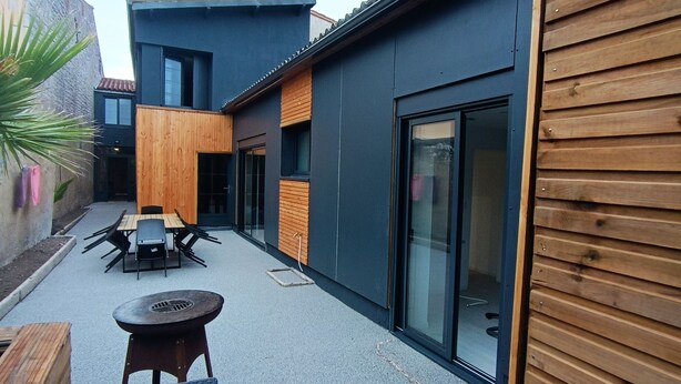 Une terrasse extérieure moderne, dotée de mobilier en bois et d’une porte vitrée donnant accès à un bâtiment.
