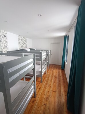 Ein Zimmer mit Etagenbetten, Holzboden, einer weißen Tür und einem Fenster mit Vorhängen.