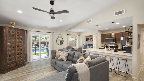 A modern living room with a grey sectional sofa, a wooden cabinet, and a kitchen area with a bar. - Kristys Kastle (Phoenix)