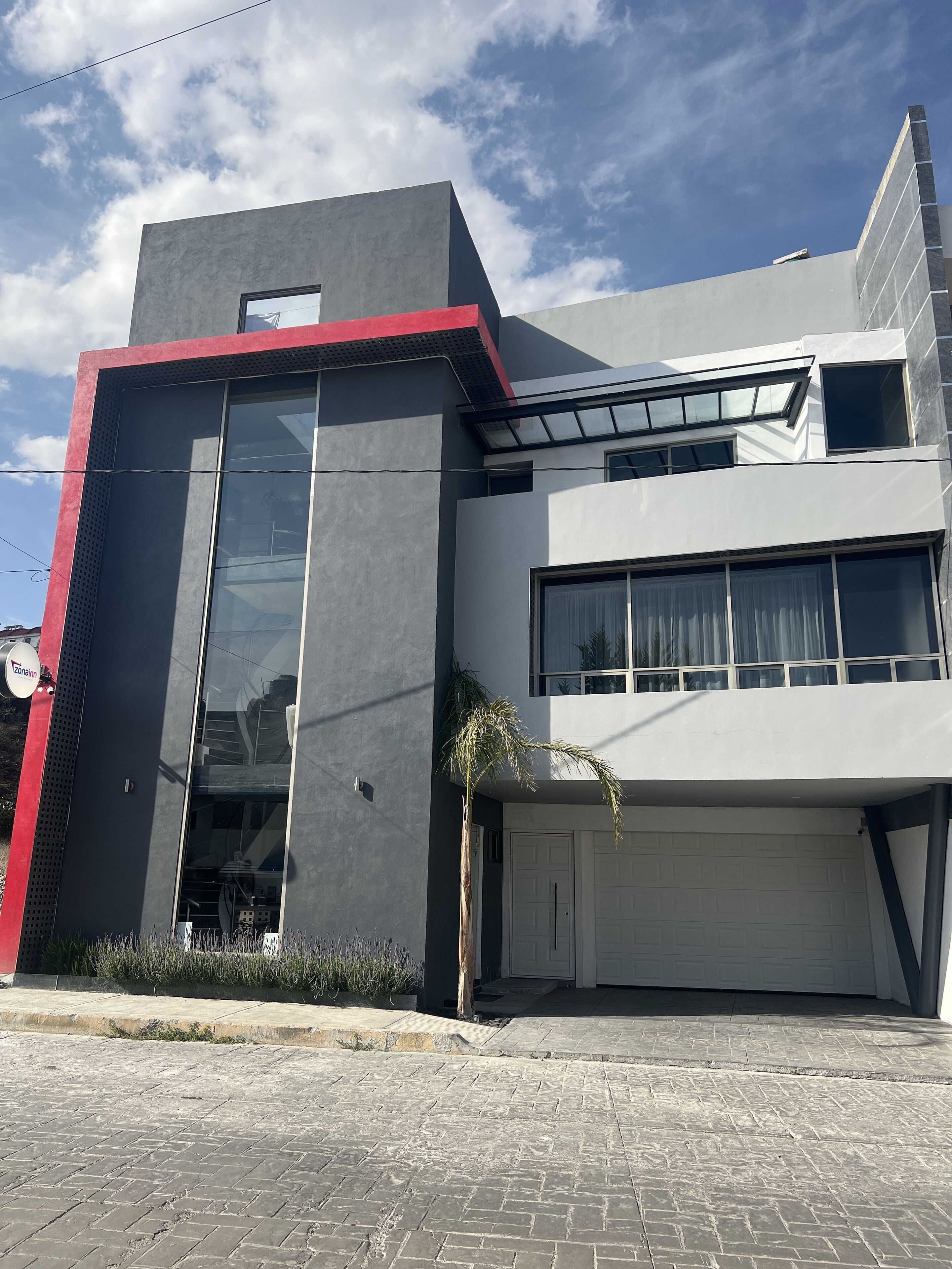 A modern two-story house with a garage, large windows, and a red accent on the facade.