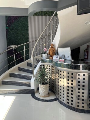 A modern reception desk with a curved staircase, a potted plant, and a statue. - Zona Inn Hotel Boutique  (Atlacomulco)